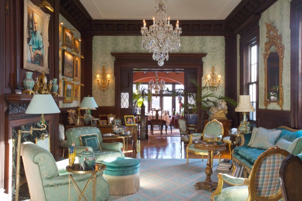 Luxurious sitting room featuring elegant decor, vintage furniture, and framed artwork. Natural light streams through large windows, enhancing the sophisticated atmosphere.