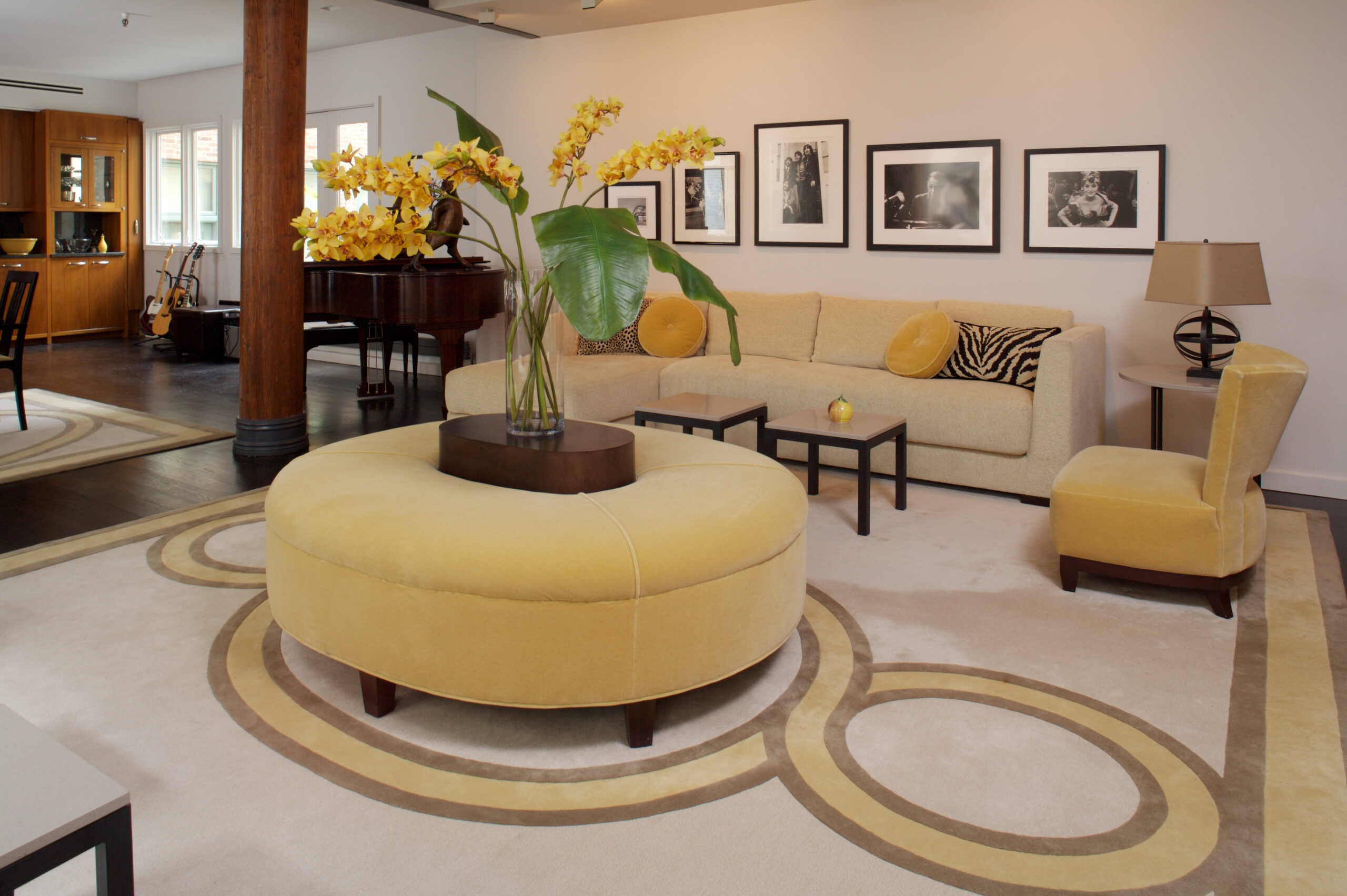 Modern living room featuring a yellow circular ottoman, a sofa, and vibrant flower arrangement. Black-and-white art adorns the walls, enhancing the aesthetic.